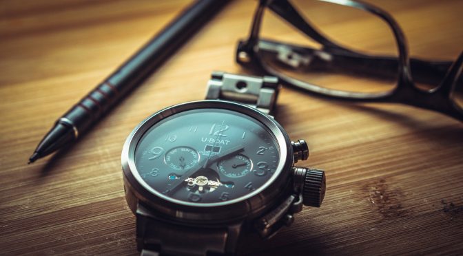 modern analogue watch next to a pair of glasses and a pen