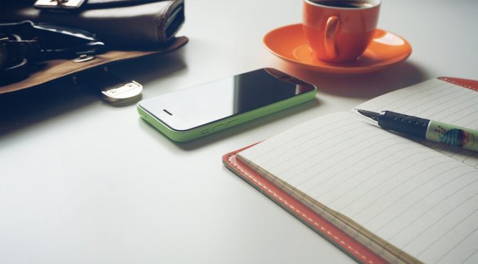 notebook and pen next to a phone and coffee cup