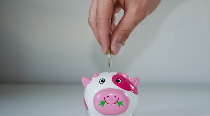 person depositing money into a small piggybank