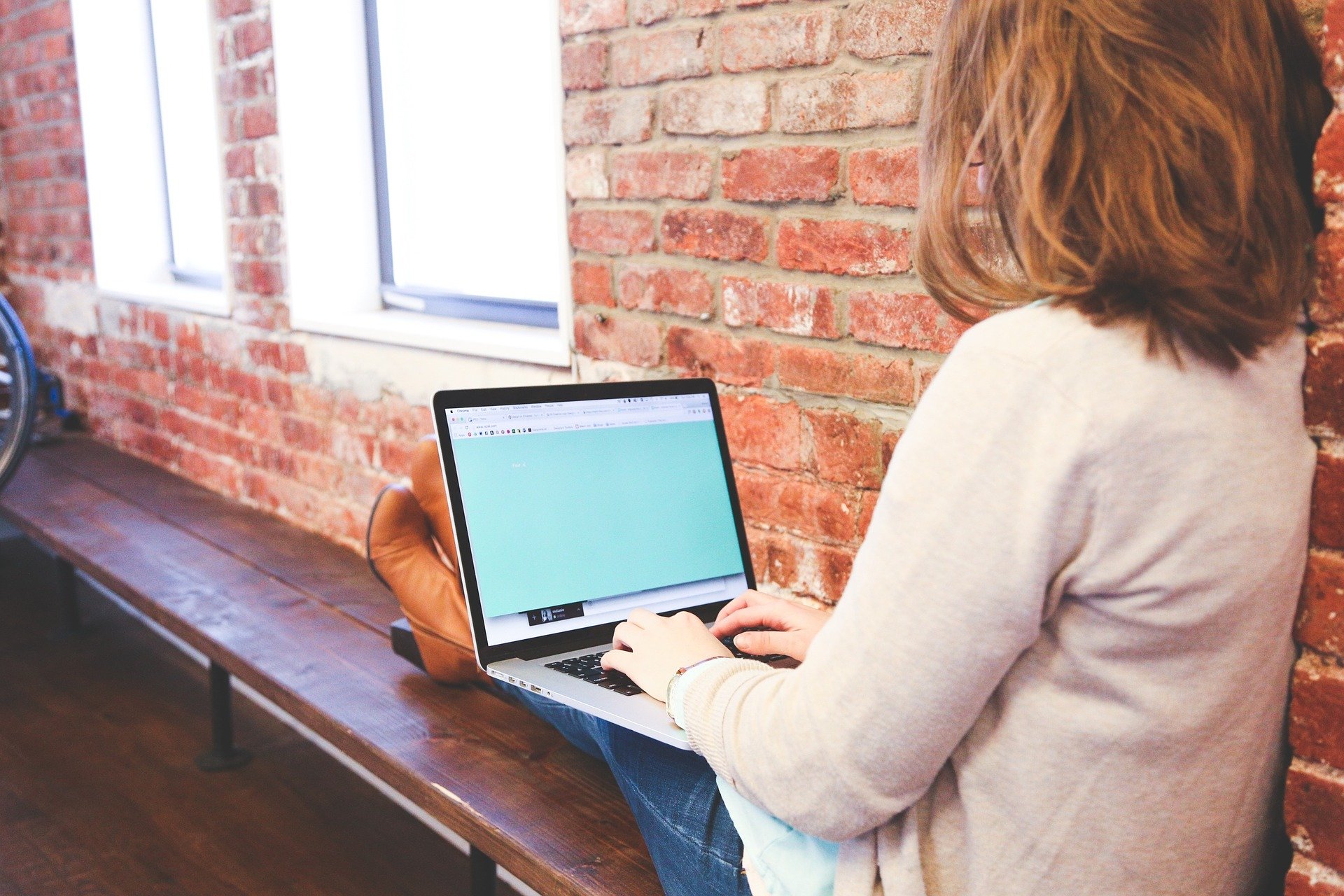 student sitting against a wall with a laptop