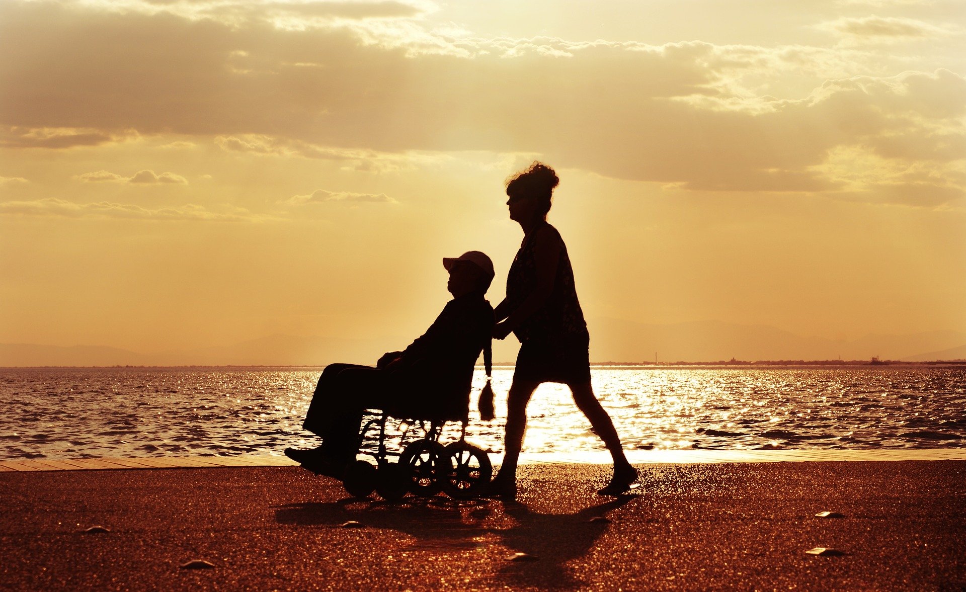 silhouette of a woman pushing a person in a wheelchair on a beach