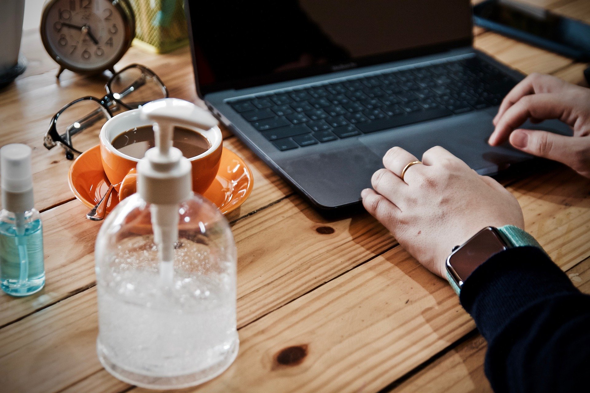 worker at their desk with a laptop, coffee, and hand sanitiser